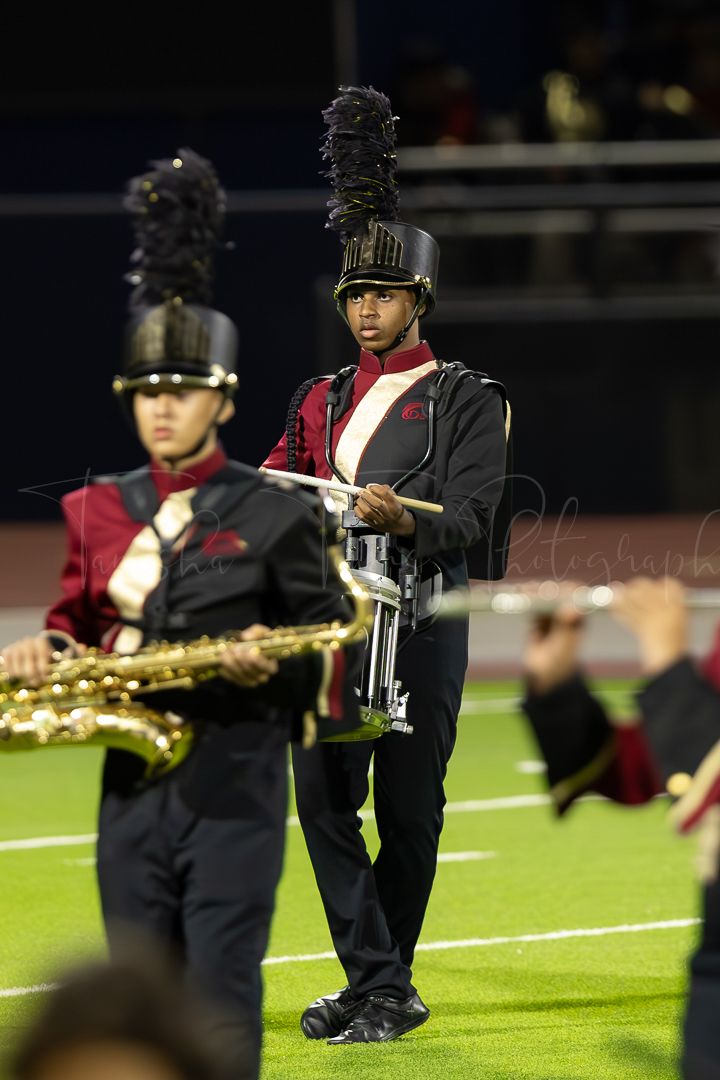Saxophone players in marching band uniforms perform on football field.