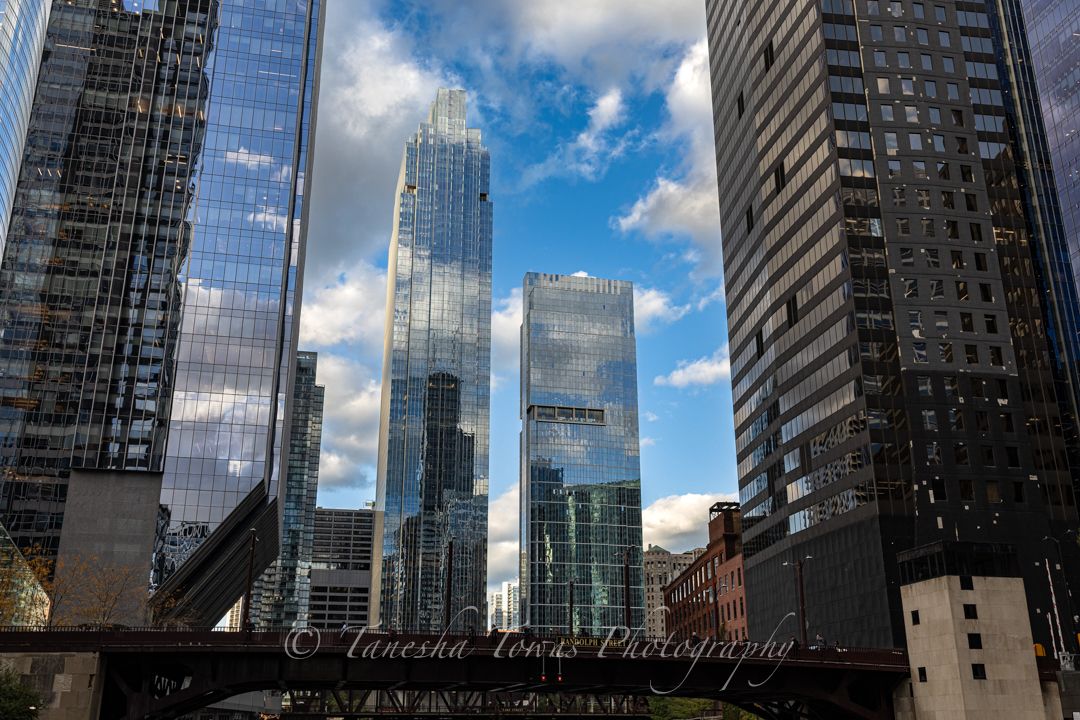 Modern glass skyscrapers reflect clouds and blue sky in a panoramic cityscape view of an urban downtown district.