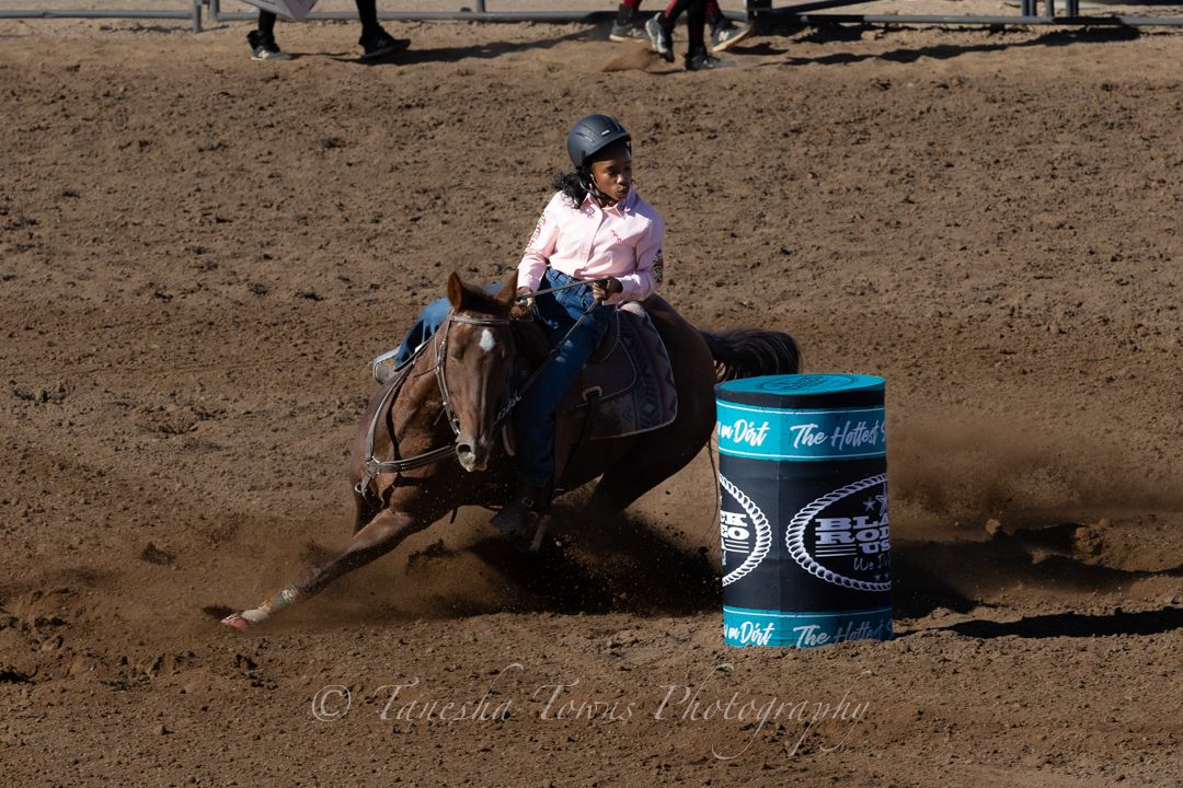 A rodeo competitor performs a barrel racing run in a dusty arena during a western competition event.