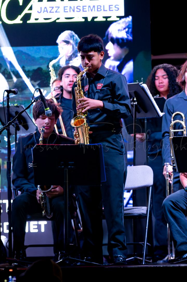 Jazz ensemble musicians in dark attire performing with saxophones and brass instruments.