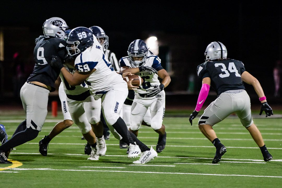 Football players engage in a ground-level play during a nighttime game on an artificial turf field.