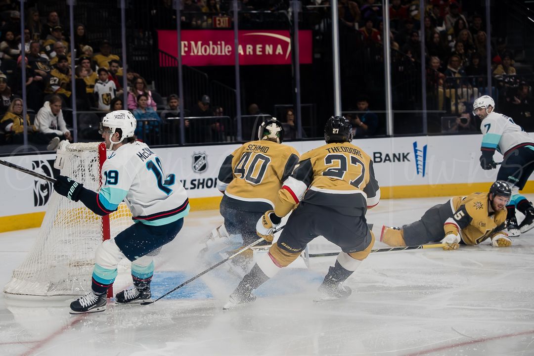 NHL players in gold and teal jerseys battle for position during an intense game sequence.