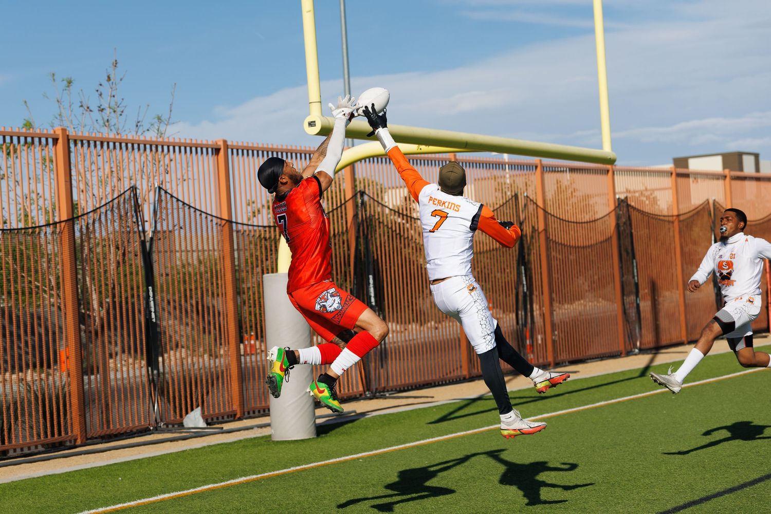 Two athletes jump near a goalpost during a competitive football game on an outdoor field.
