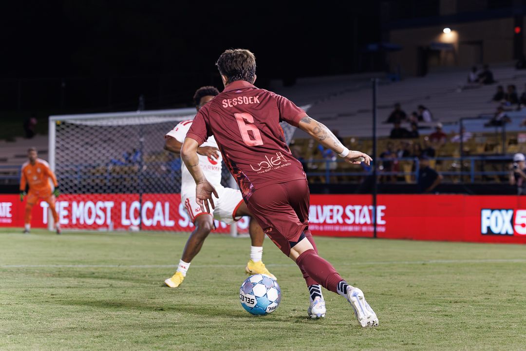 Soccer player number 6 in maroon uniform controls the ball during a competitive night match.