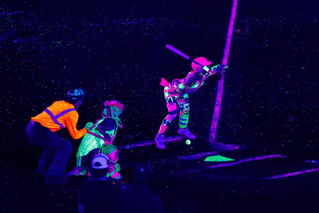 Players glow under black lights during a neon-themed nighttime baseball game.