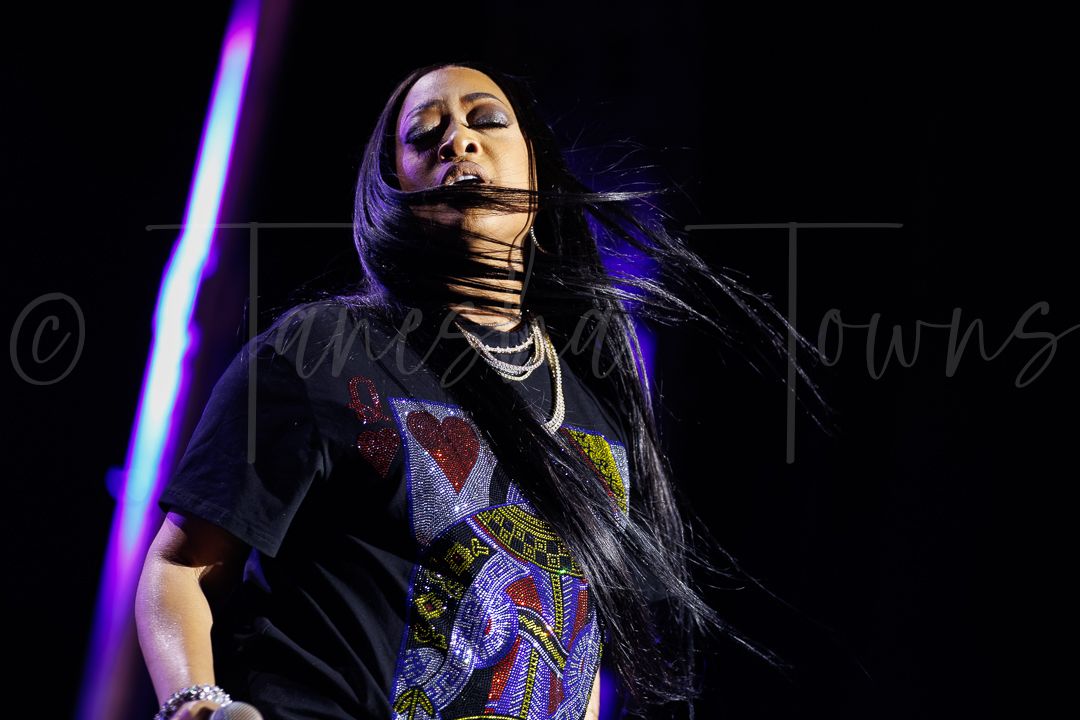 Female singer performing on stage with hair flowing, wearing colorful graphic tee under blue stage lights.