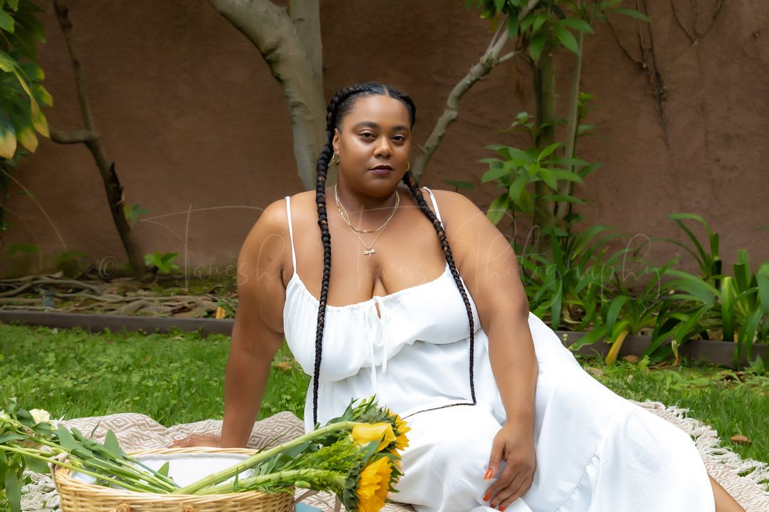 A person in white lounges on grass with sunflowers and greenery in the background.