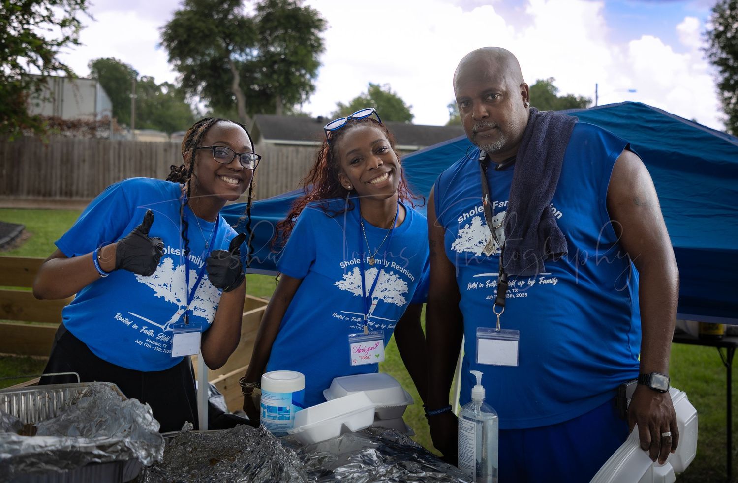 Group of people in matching blue t-shirts gather at an outdoor event.