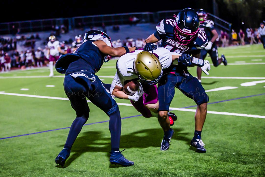Football defenders tackle ball carrier during intense nighttime game action.