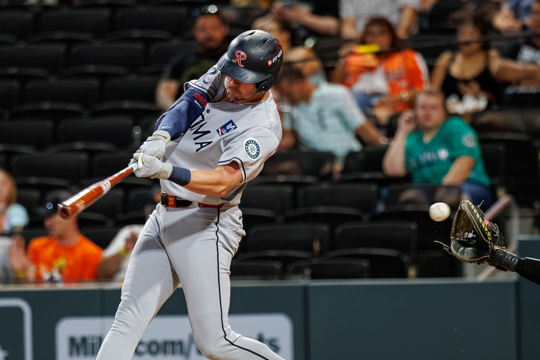 A Tacoma baseball player swings at a pitch during a night game, making contact with the ball at home plate.