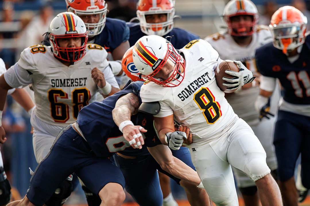 Somerset player #8 is tackled during a high school football game against a blue-uniformed opponent on the field.