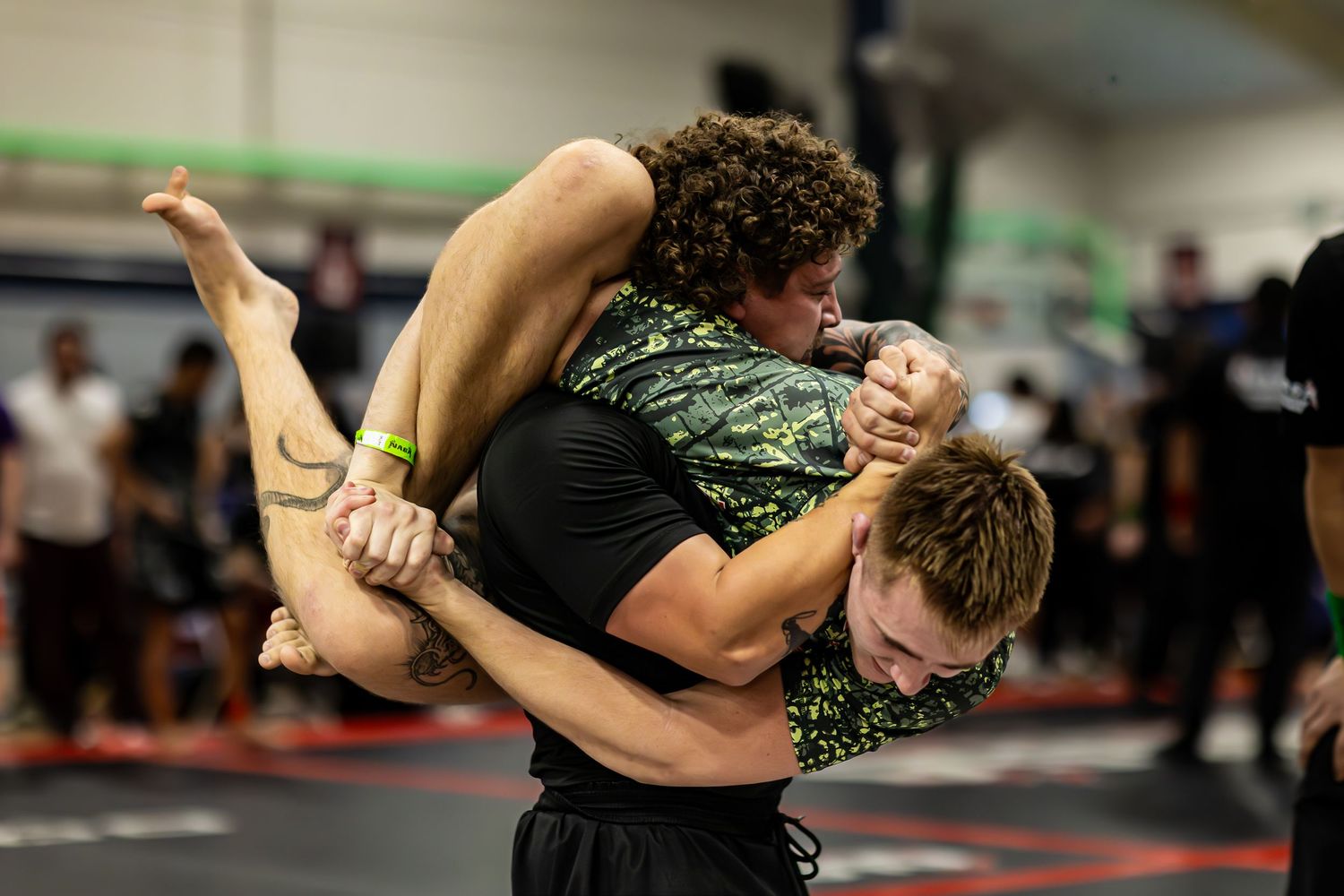Two wrestlers grappling on a mat during a submission wrestling match at an indoor martial arts gym.