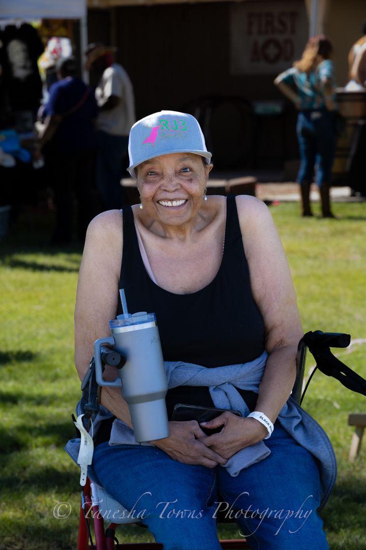 Person in a baseball cap and black tank top sits outdoors holding a water bottle on a sunny day.