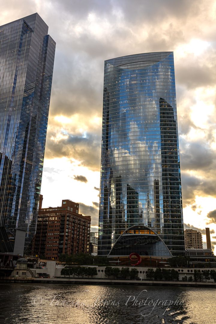 Modern glass skyscraper reflecting dramatic sunset clouds along Chicago's riverfront at dusk.