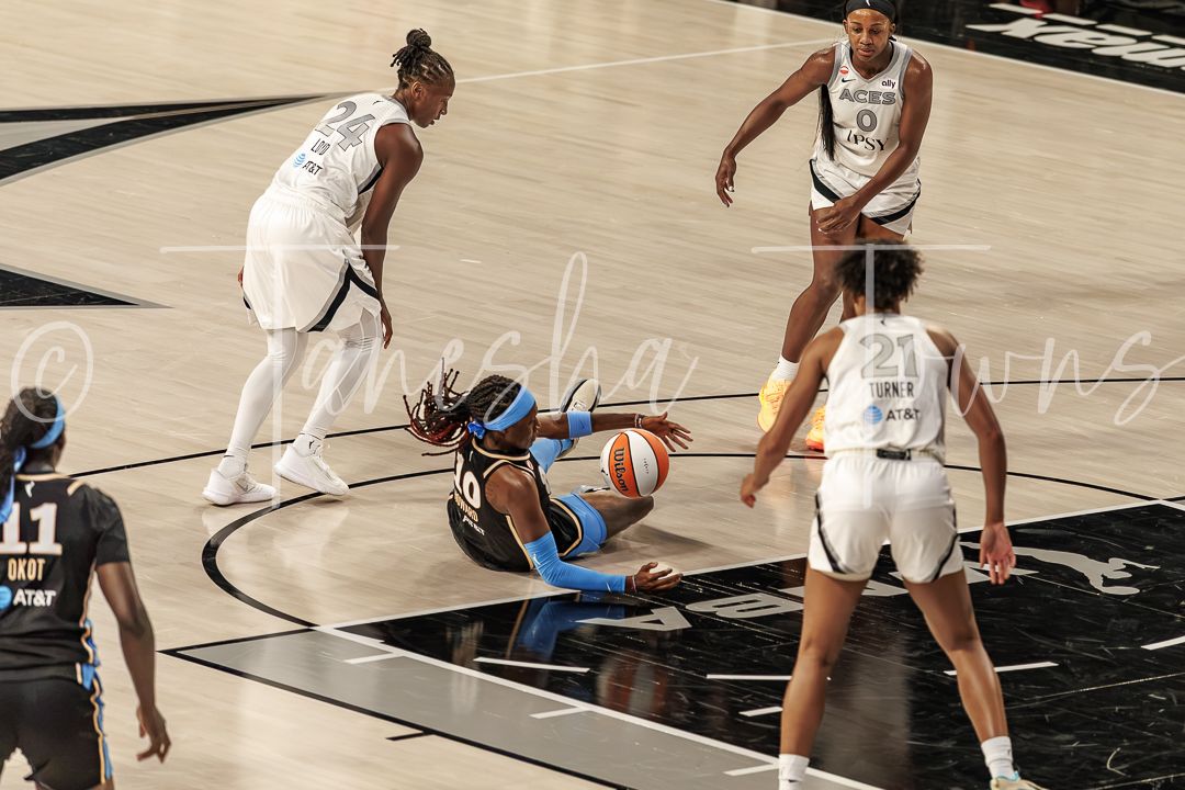 WNBA player diving for loose ball during game, surrounded by teammates in white and blue uniforms on indoor court.