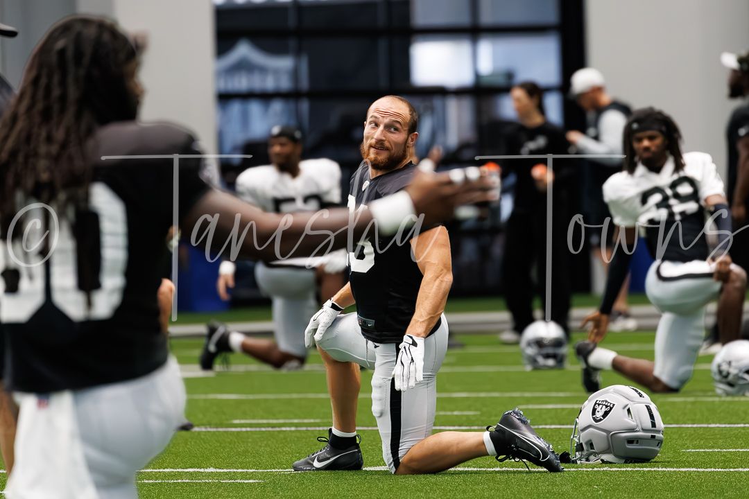 Las Vegas Raiders player stretches on turf during indoor training camp practice session.