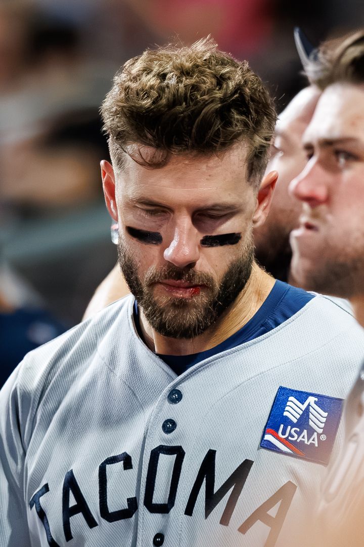 A Tacoma baseball player with eye black looks down in the dugout wearing a gray uniform with USAA sponsor patch.