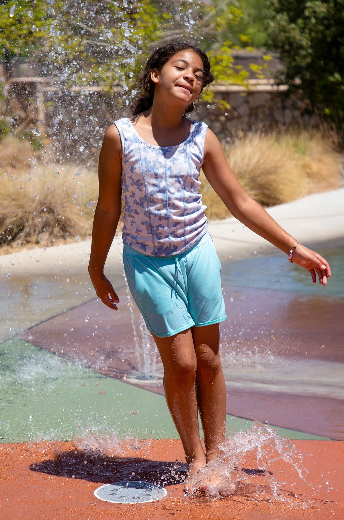 Child playing and splashing in water at an outdoor splash pad.