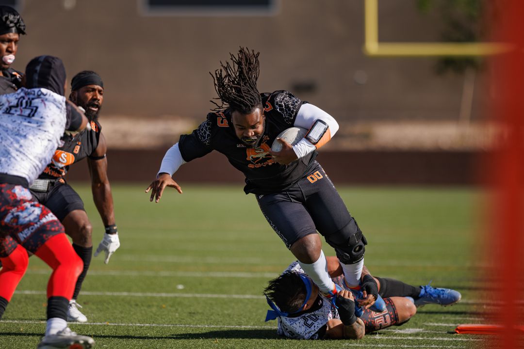 Football player with dreadlocks breaks through tackle during outdoor game.