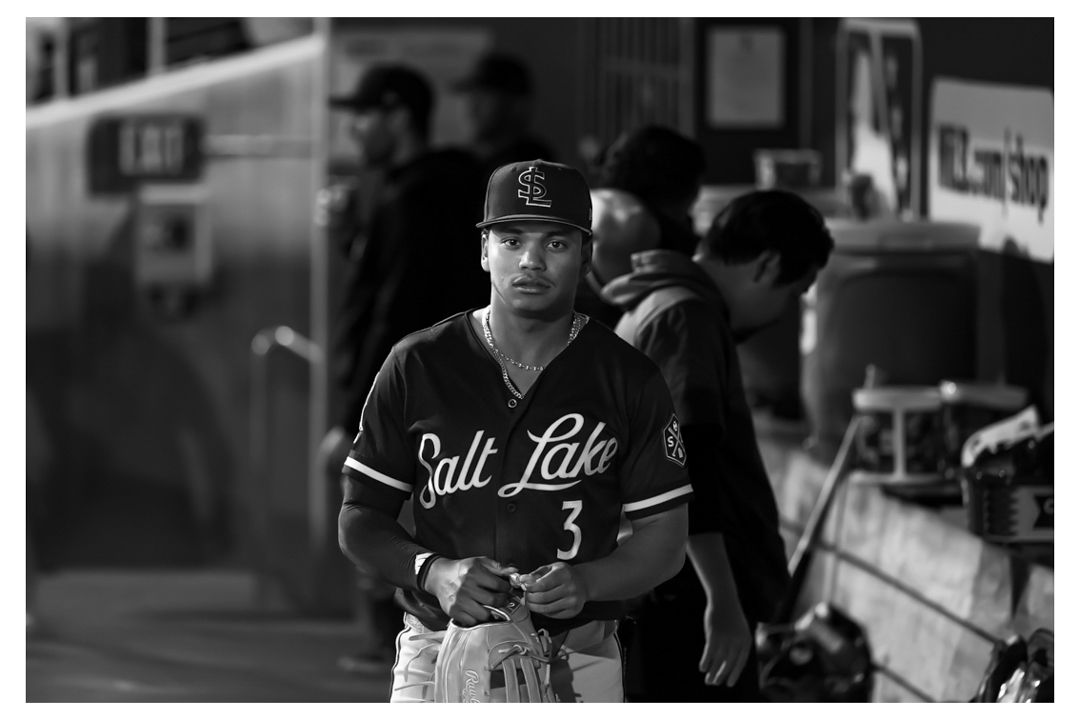 Salt Lake Bees player #3 stands in dugout during a baseball game in black and white photo.