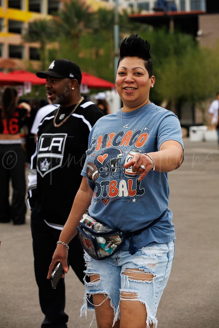 Woman in Chicago Football t-shirt and ripped jeans smiling outdoors at a sports event.
