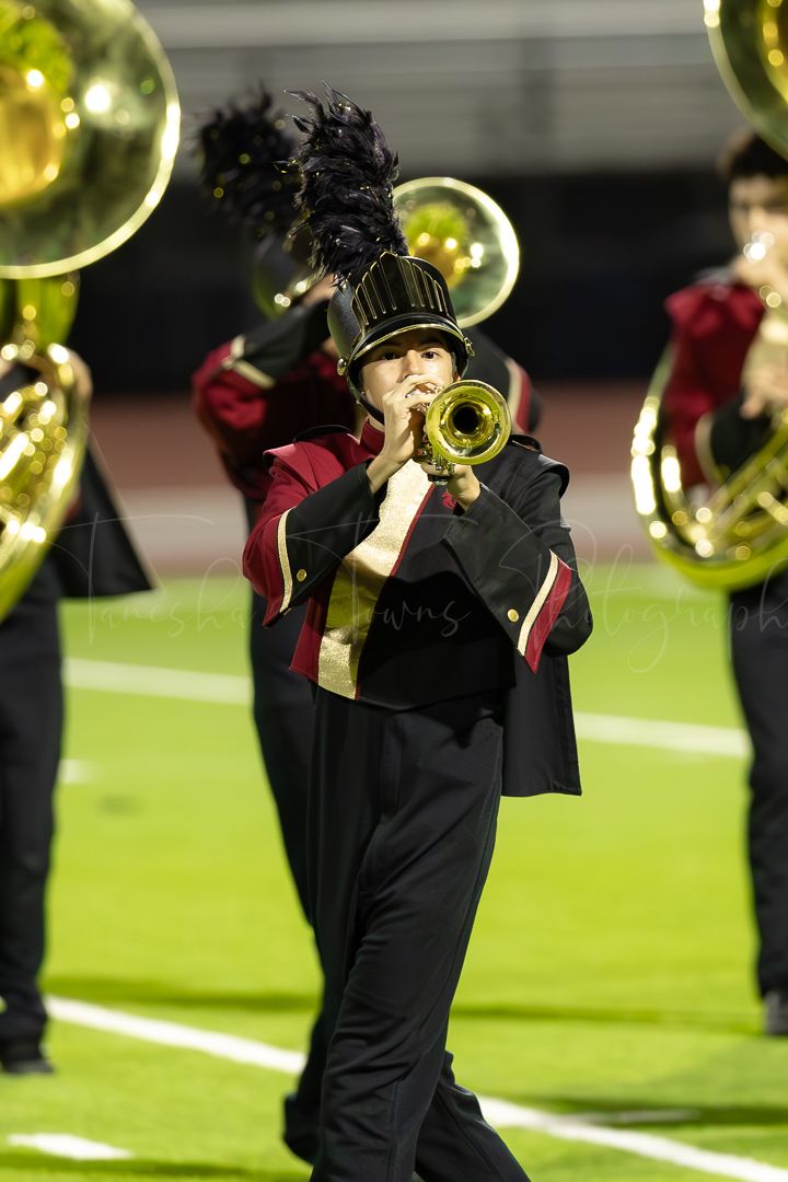 Sousaphone players in black uniforms perform during a nighttime marching band show.