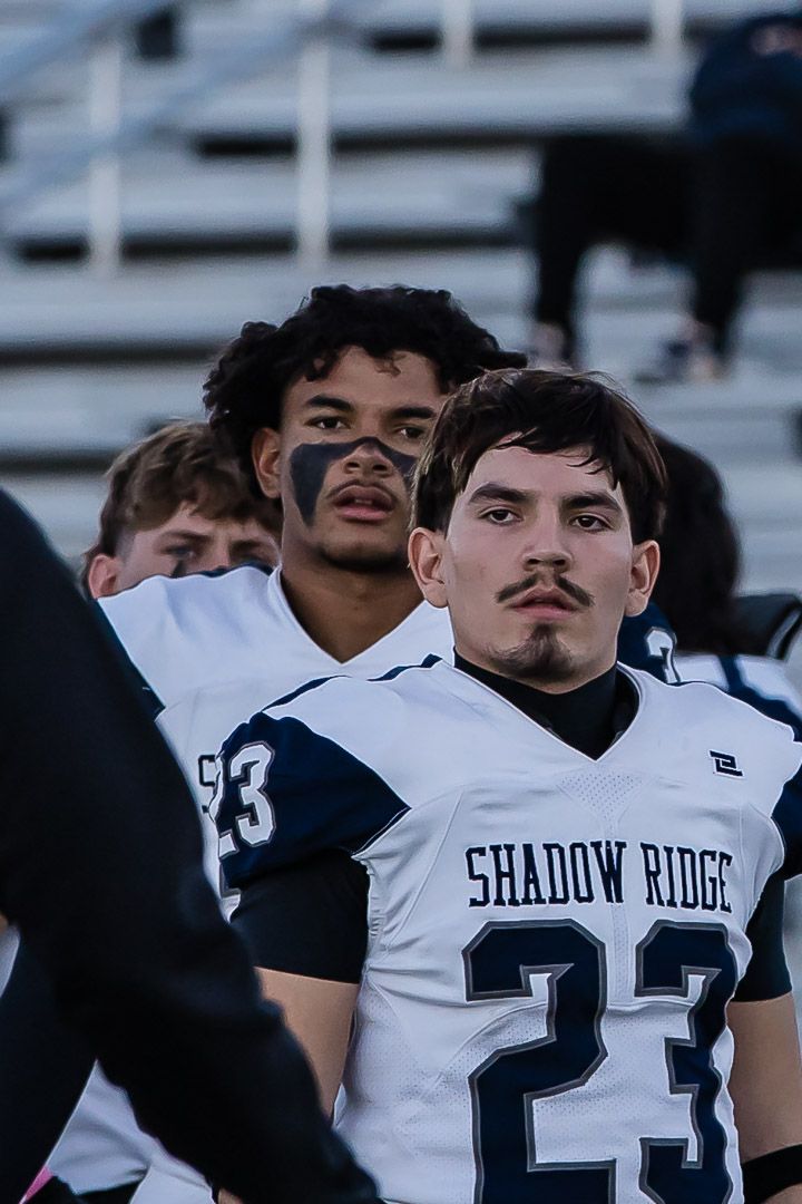 Shadow Ridge football players in white uniforms on the sidelines during a game.