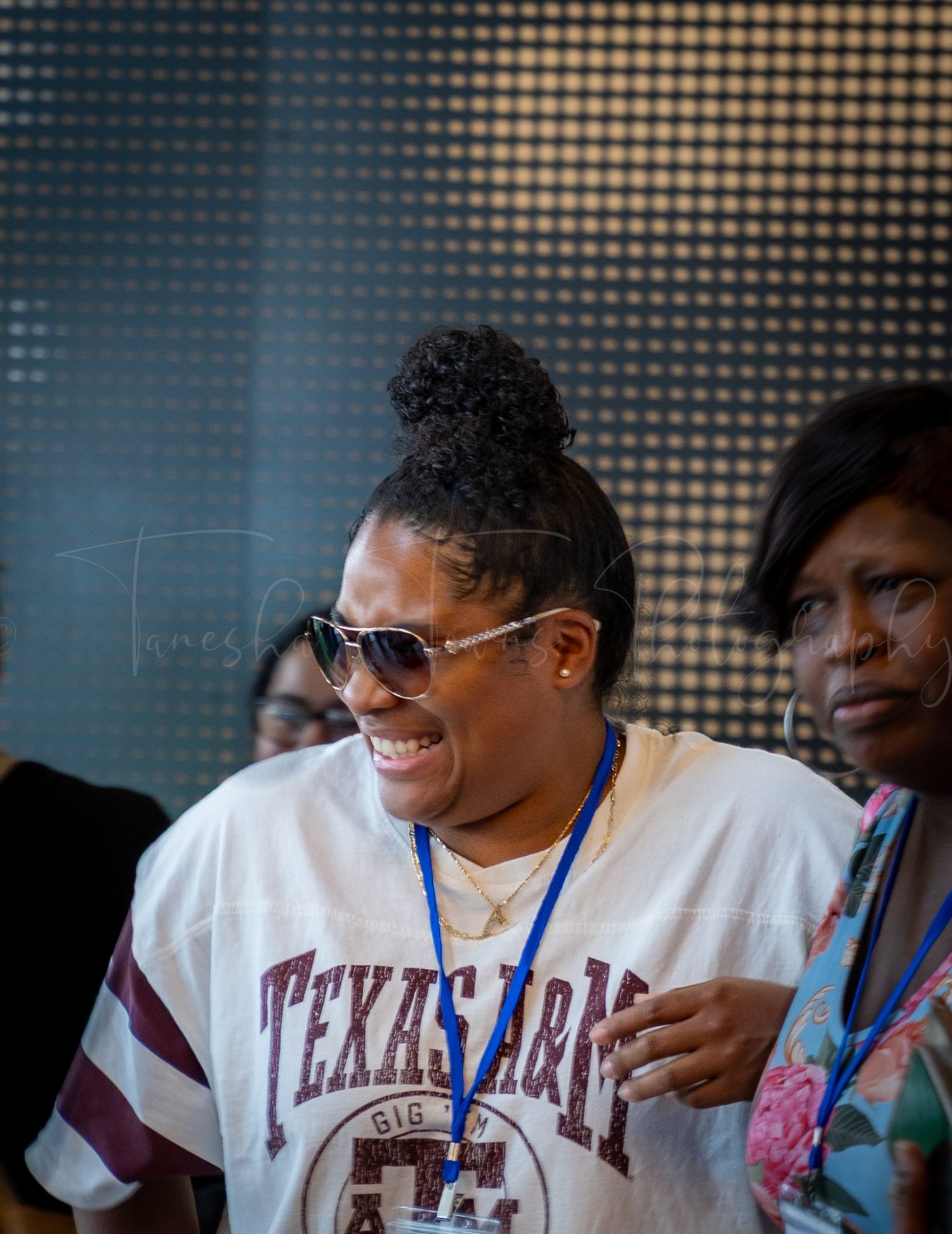 Person wearing a Texas A&M shirt and sunglasses smiling at an indoor event.