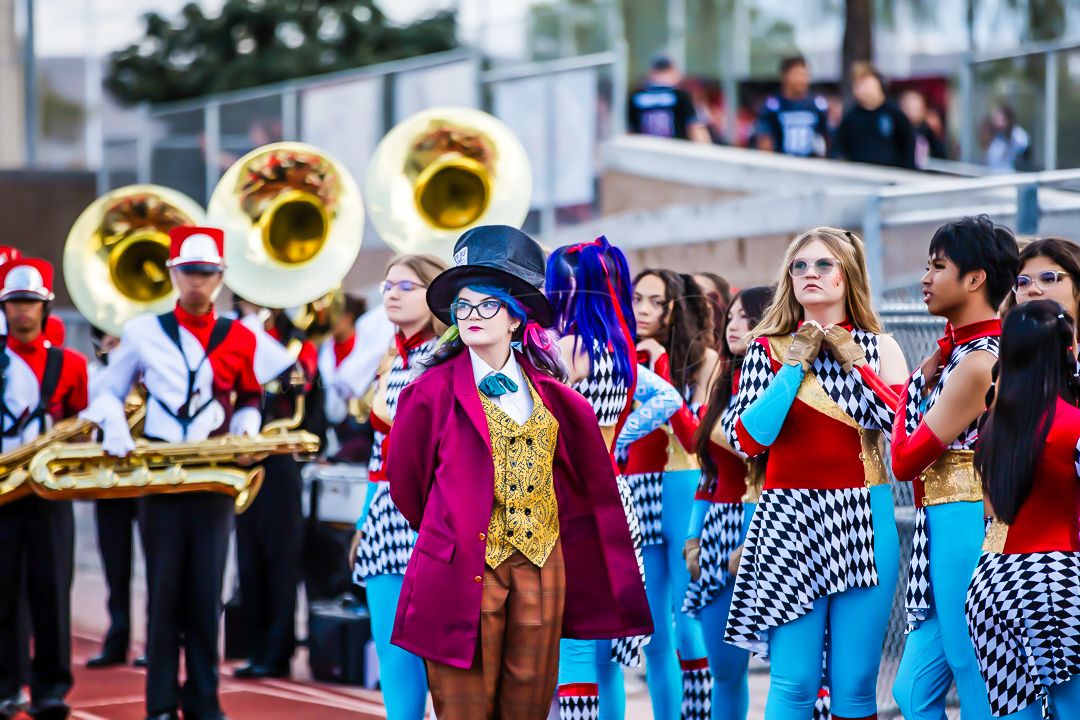 Marching band members perform in colorful uniforms with brass instruments on field.
