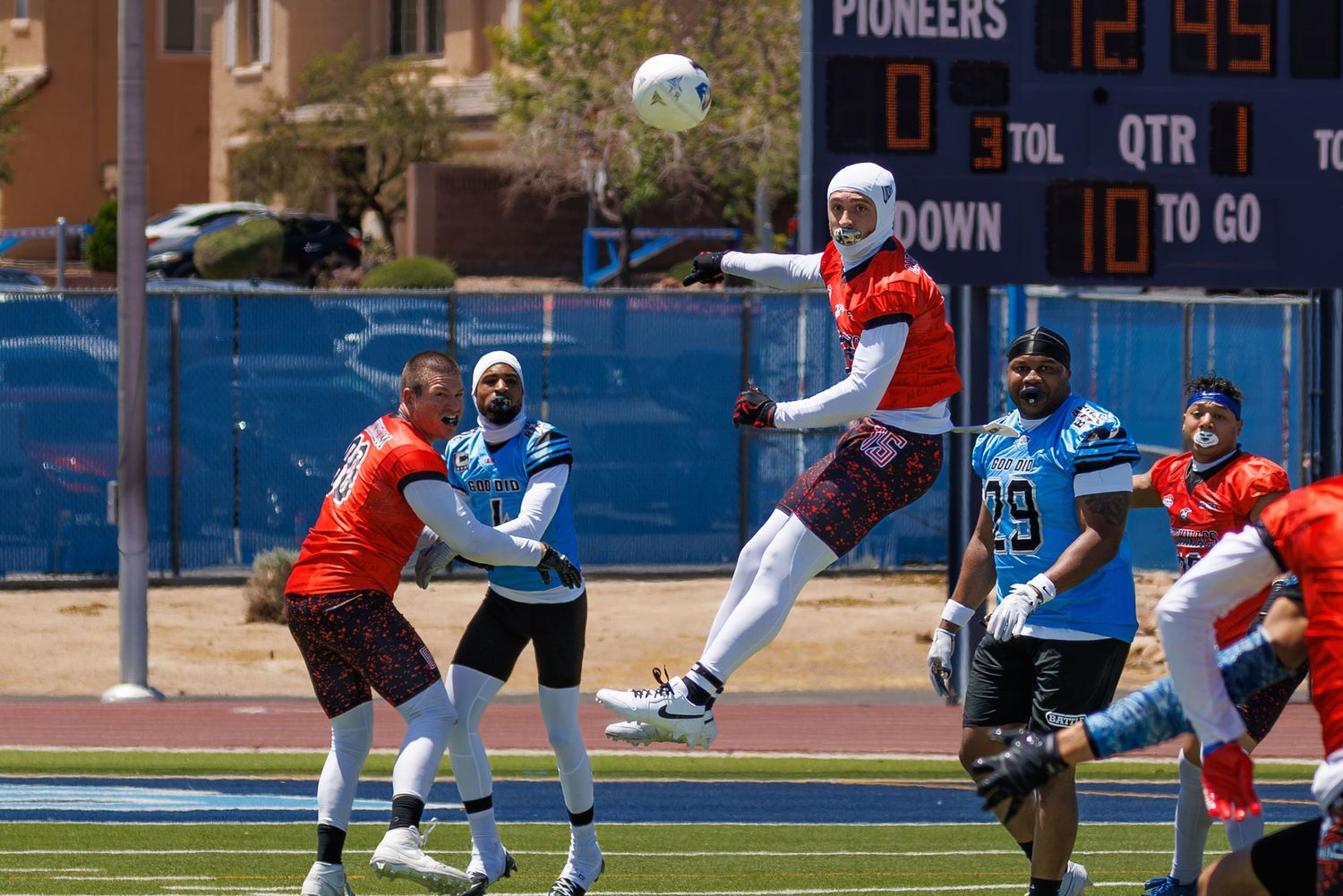 Athletes compete in a flag football game on a blue turf field, with a scoreboard showing Pioneers in the background.