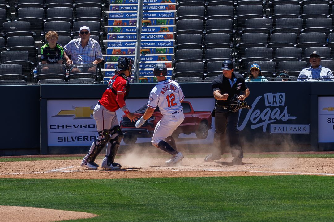 Baseball batter swings at pitch near home plate as catcher and umpire watch during Las Vegas Aviators game.