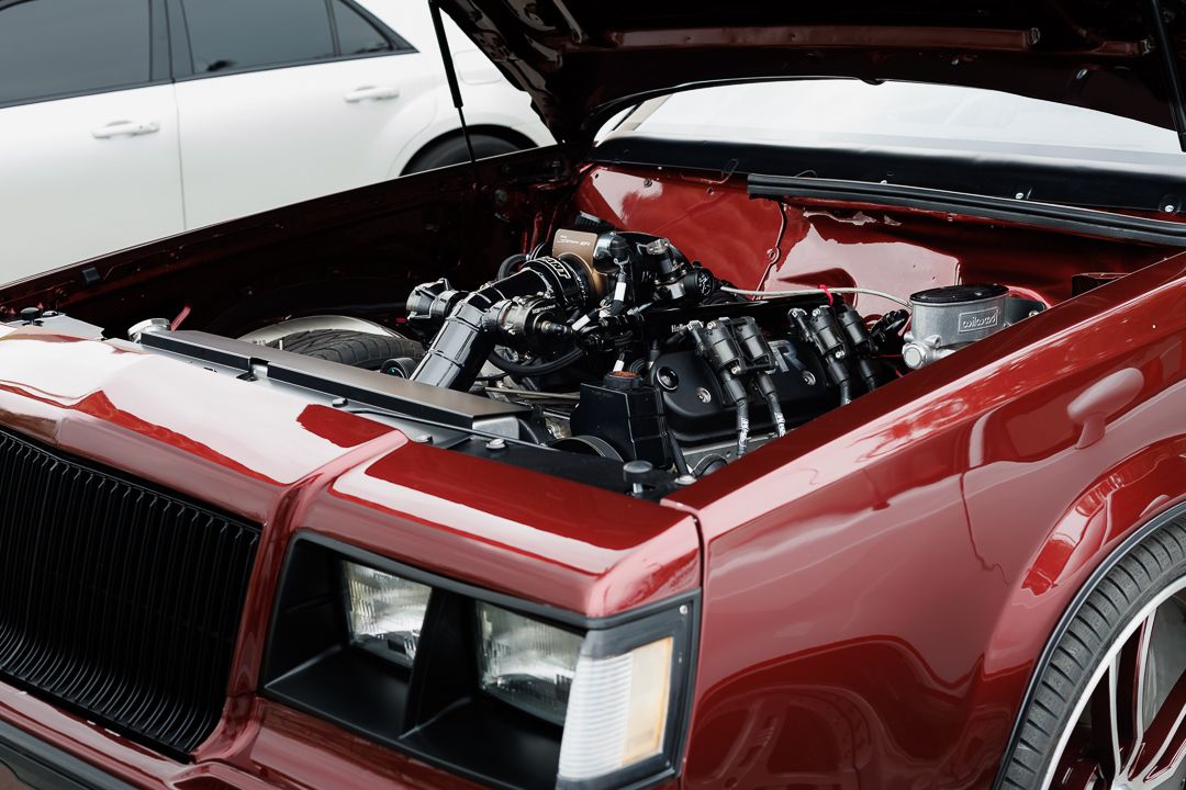 Red classic car with open hood revealing a detailed black engine bay.