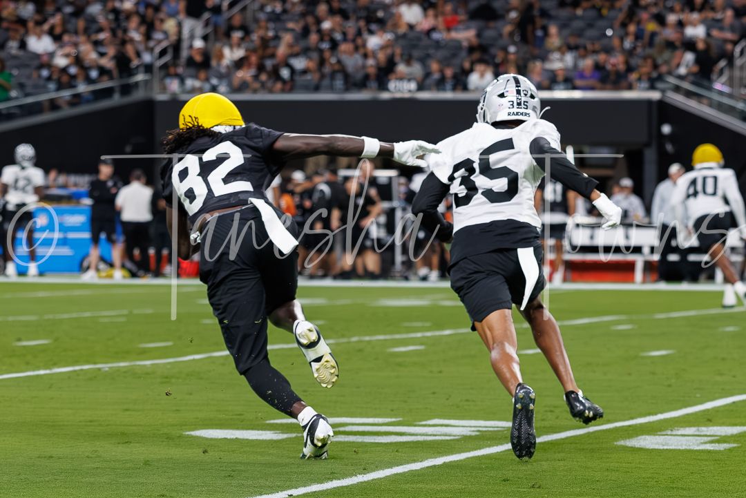Football player #82 attempts a catch while defended by player #35 during a night game at a modern stadium.
