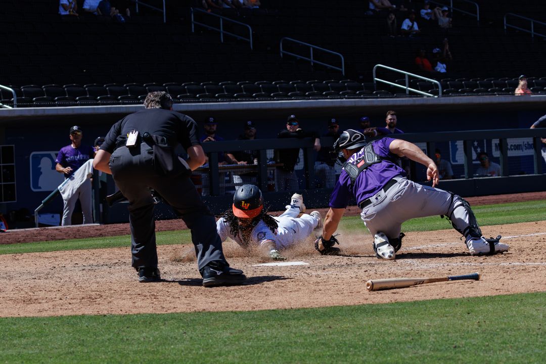 Baseball player slides into home plate as catcher attempts a tag while umpire watches the play closely.