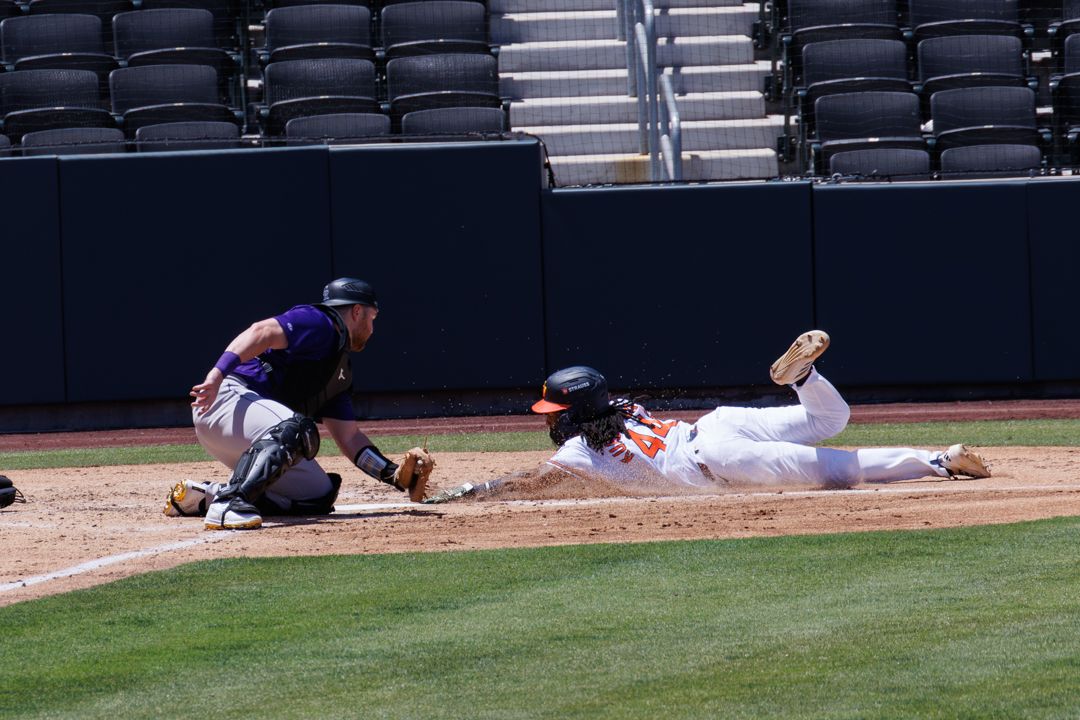 A baseball player in orange uniform slides into home plate as the catcher attempts a tag.