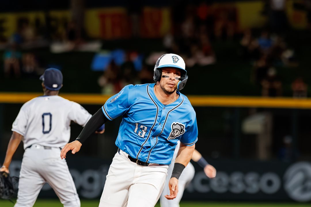 Baseball player in blue uniform rounds the bases during a night game.