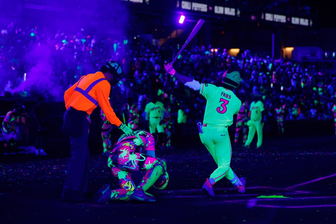 Performers in neon costumes under black lights at a vibrant concert event with colorful UV-reactive outfits.