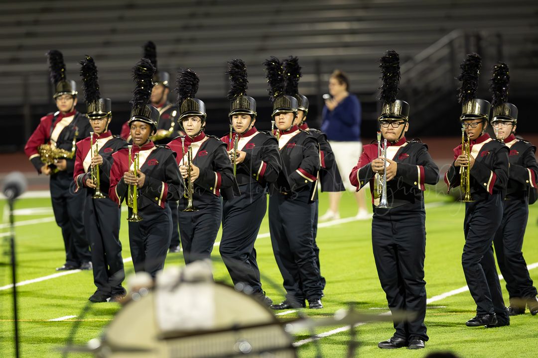 Marching band members lined up in black uniforms on a football field.