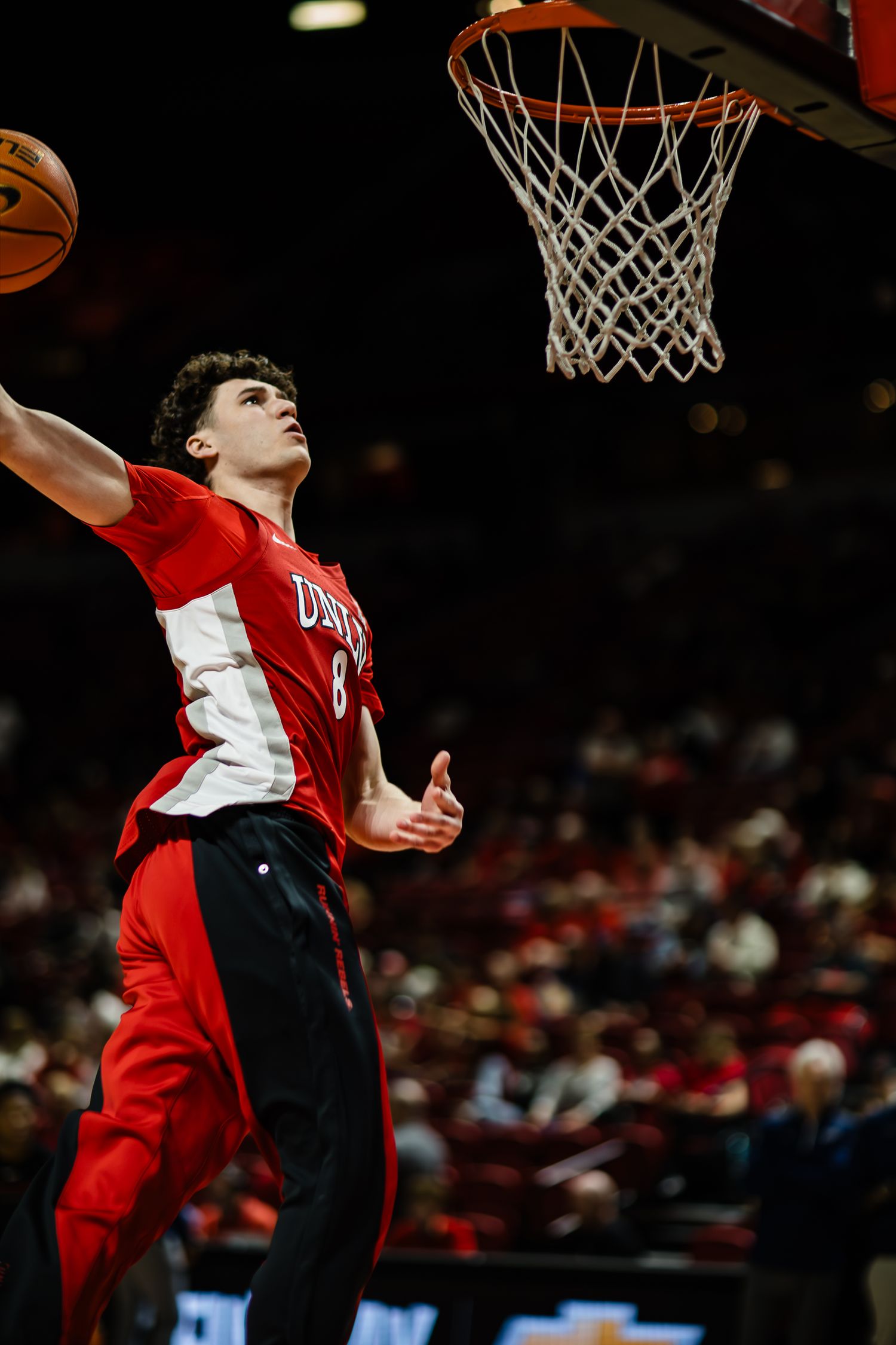 Basketball player in red jersey #8 drives to the hoop for a layup during a college game.