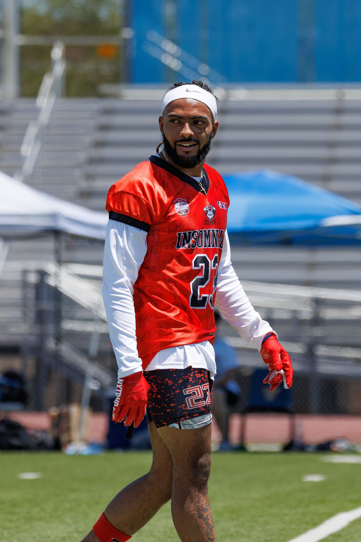 A smiling football player in a red Insomnia jersey number 22 walks on the field during a sunny outdoor game.