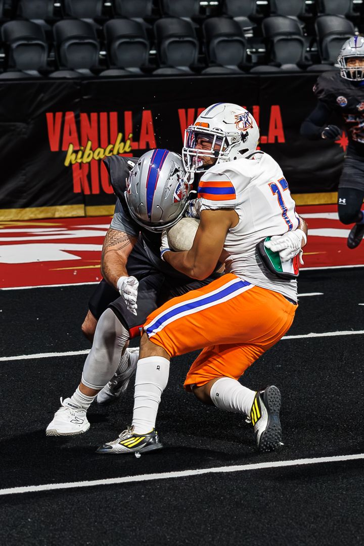 Two indoor football players collide near the end zone during an arena football game.
