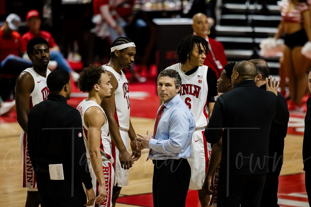 Basketball players and coaches gather on the sideline during an intense game in a packed arena.
