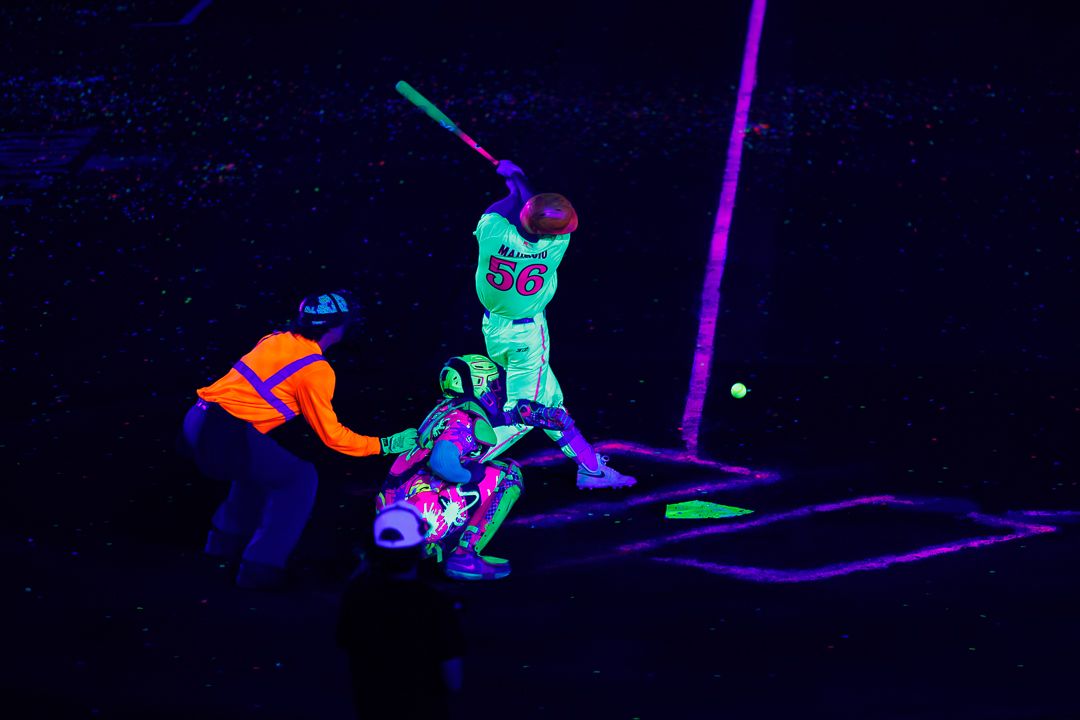 Batter swings at a pitch under black light during a neon glow-in-the-dark baseball game.
