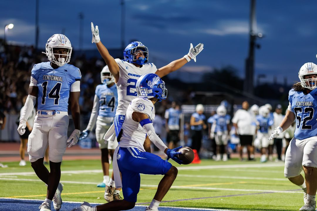 High school football players celebrate a touchdown during a night game under stadium lights.