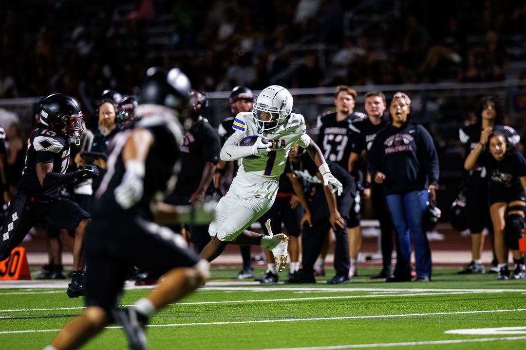 Football player in white uniform runs with the ball during a night game under stadium lights.