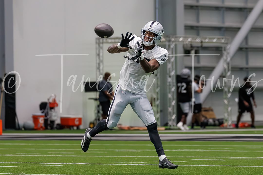 Football player catching a pass during an indoor practice session at an NFL training facility.
