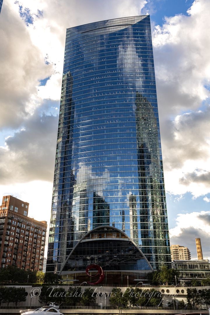 Curved glass facade of modern Chicago office building reflects clouds and sunlight against urban skyline.