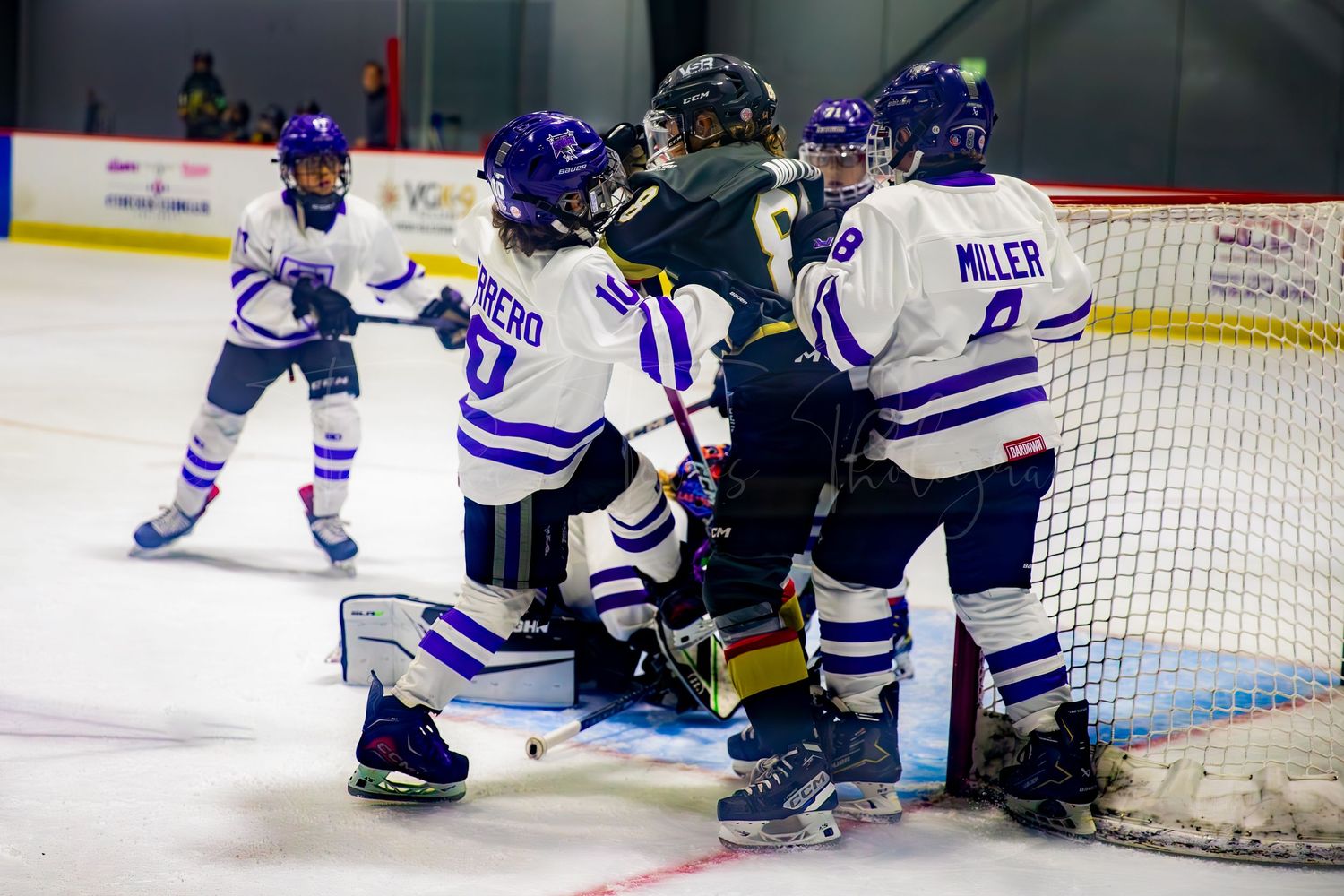 Hockey players in blue and white striped jerseys crowd around the goal net during game action.