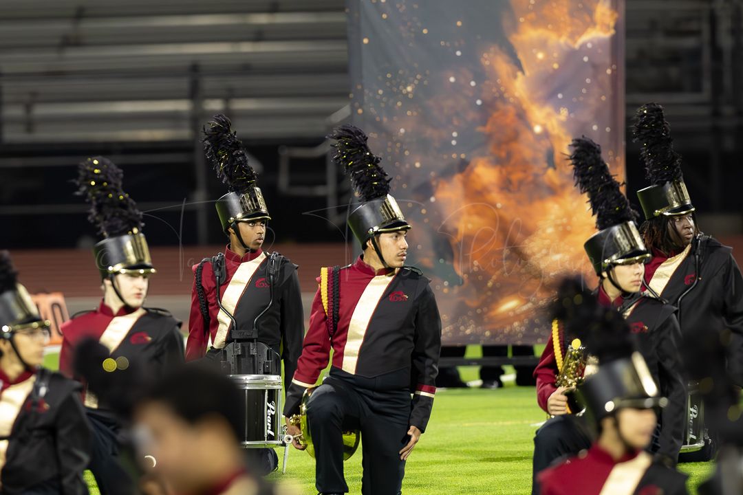 Marching band performs at night with dramatic fire effects in background.