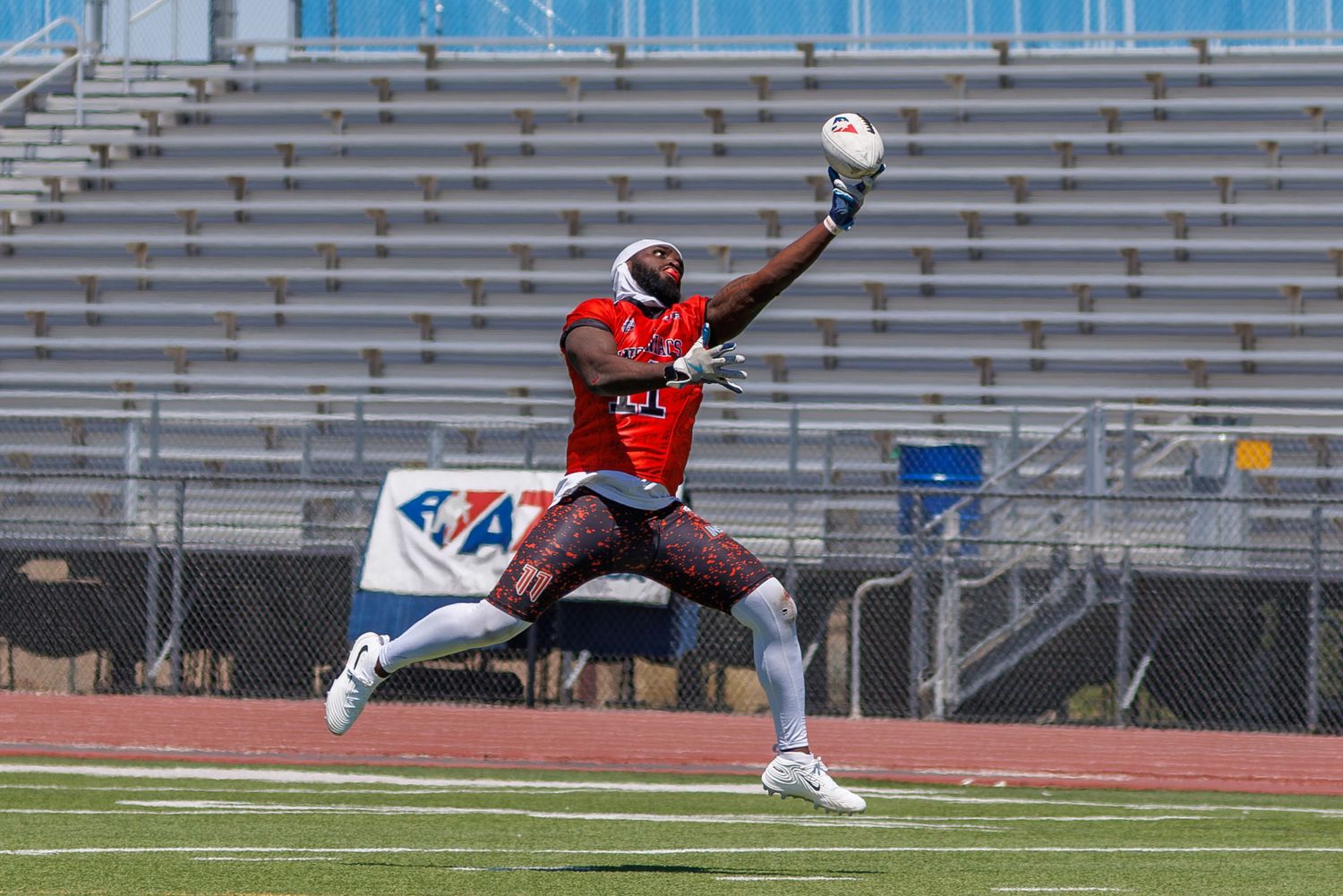 Football player in red uniform leaps to make a one-handed catch during an outdoor stadium game.